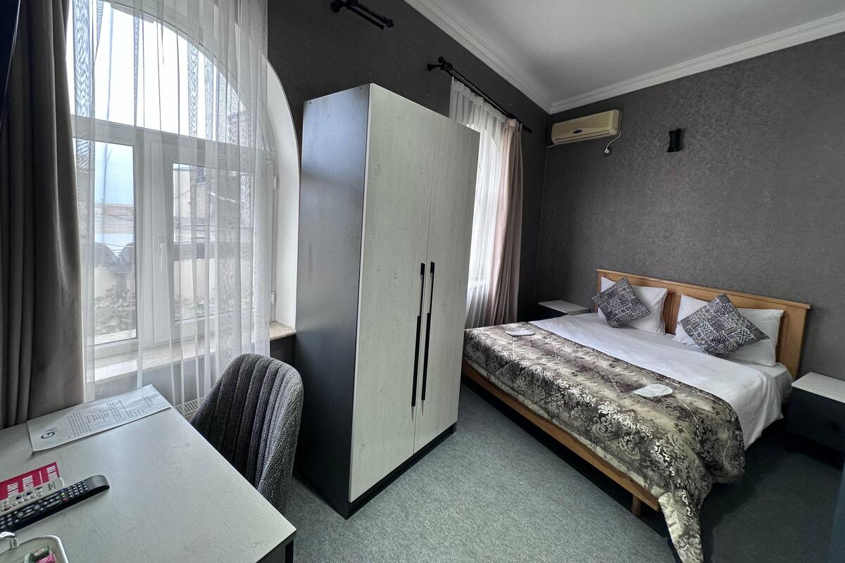 Une chambre d’hôtel avec un lit, un bureau, une armoire et une fenêtre avec des rideaux.