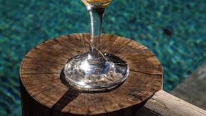 A cocktail in a glass with a tropical garnish, placed on a wooden stump by a pool. - Villa Das contas Boutique  (Itacaré)
