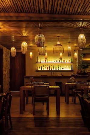 A bar area with wooden ceiling, multiple hanging light fixtures, and a shelf with bottles. - Villa Das contas Boutique  (Itacaré)