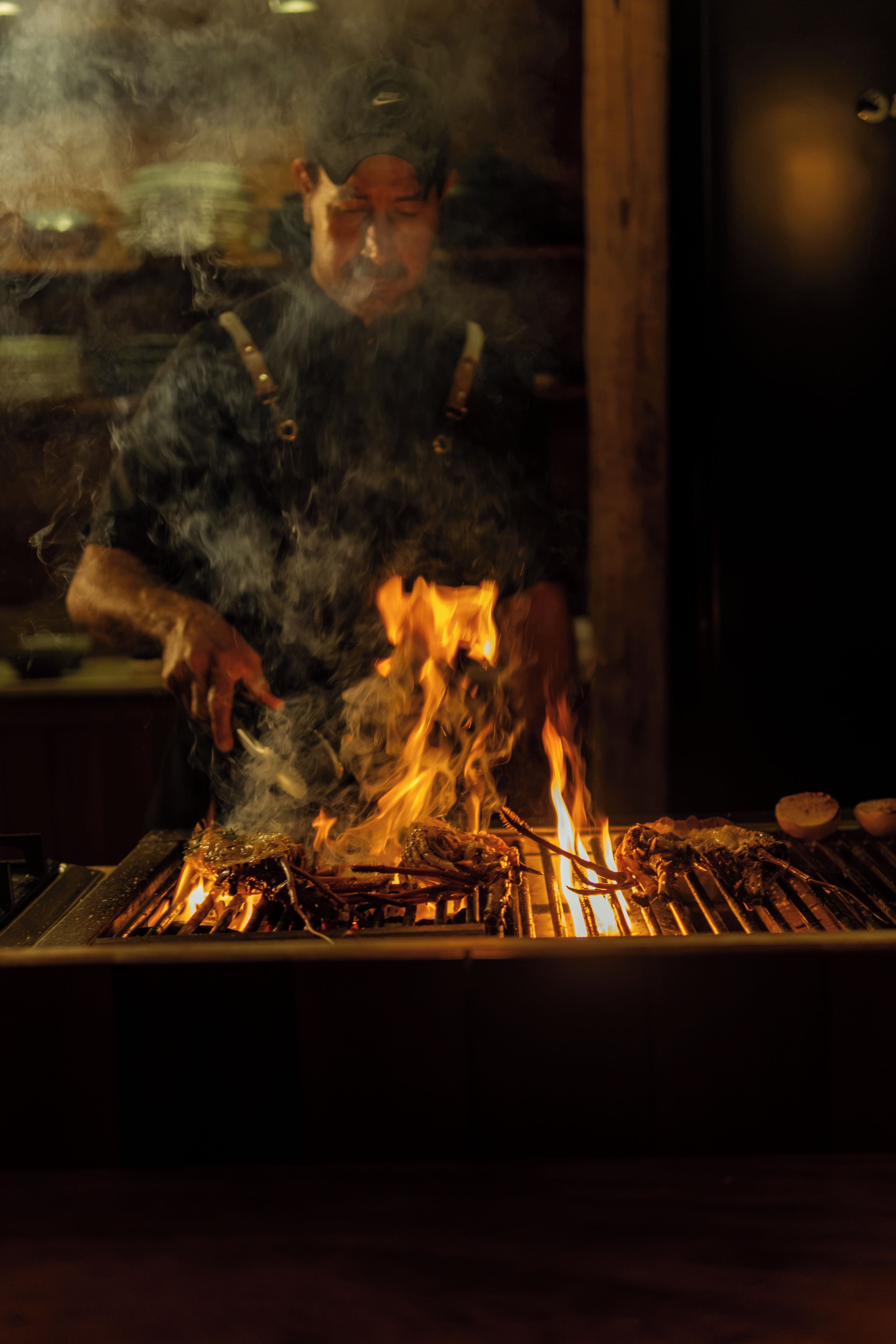 Un cocinero asando comida en una parrilla con llamas visibles.