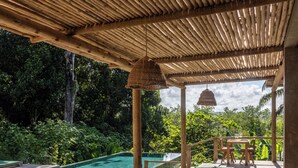 A wooden deck with a pool, green cushioned seating, and a hanging light fixture. - Villa Das contas Boutique  (Itacaré)