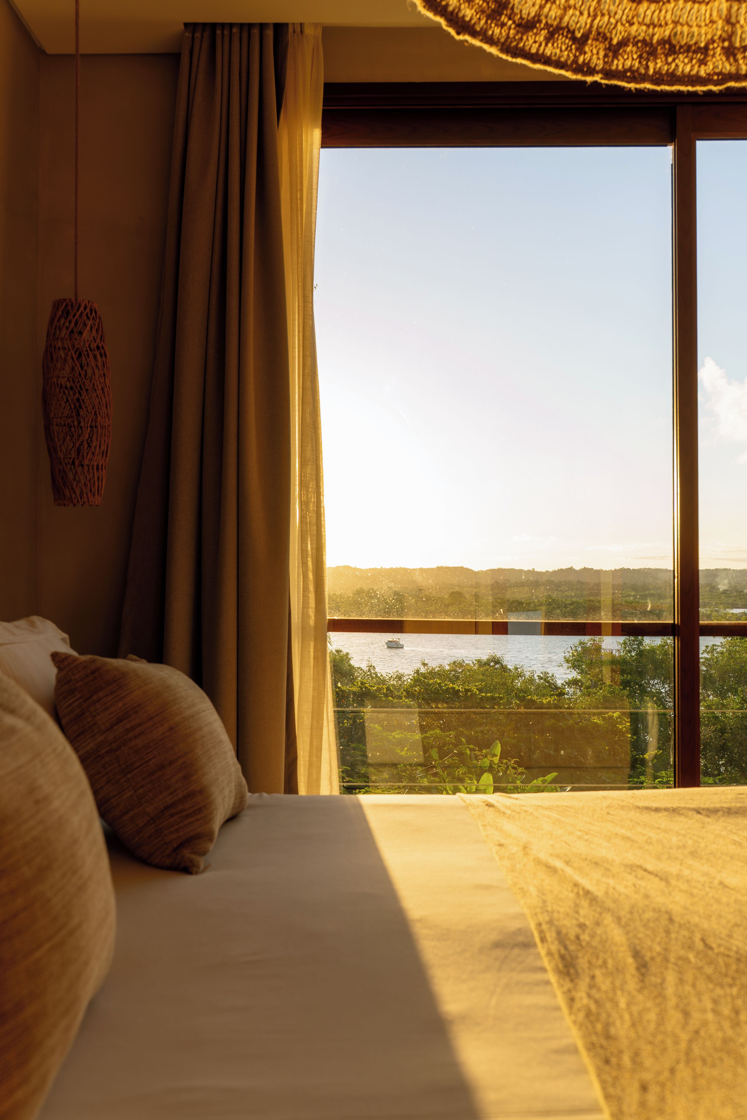 Ein Schlafzimmer mit großem Fenster, einem Bett und Blick auf Wasser und Grünflächen.