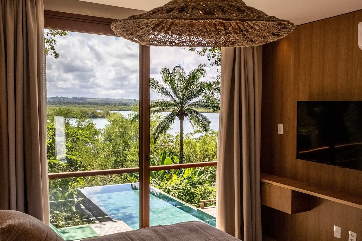 A bedroom with a large bed, a TV, and a view of a pool and palm tree.