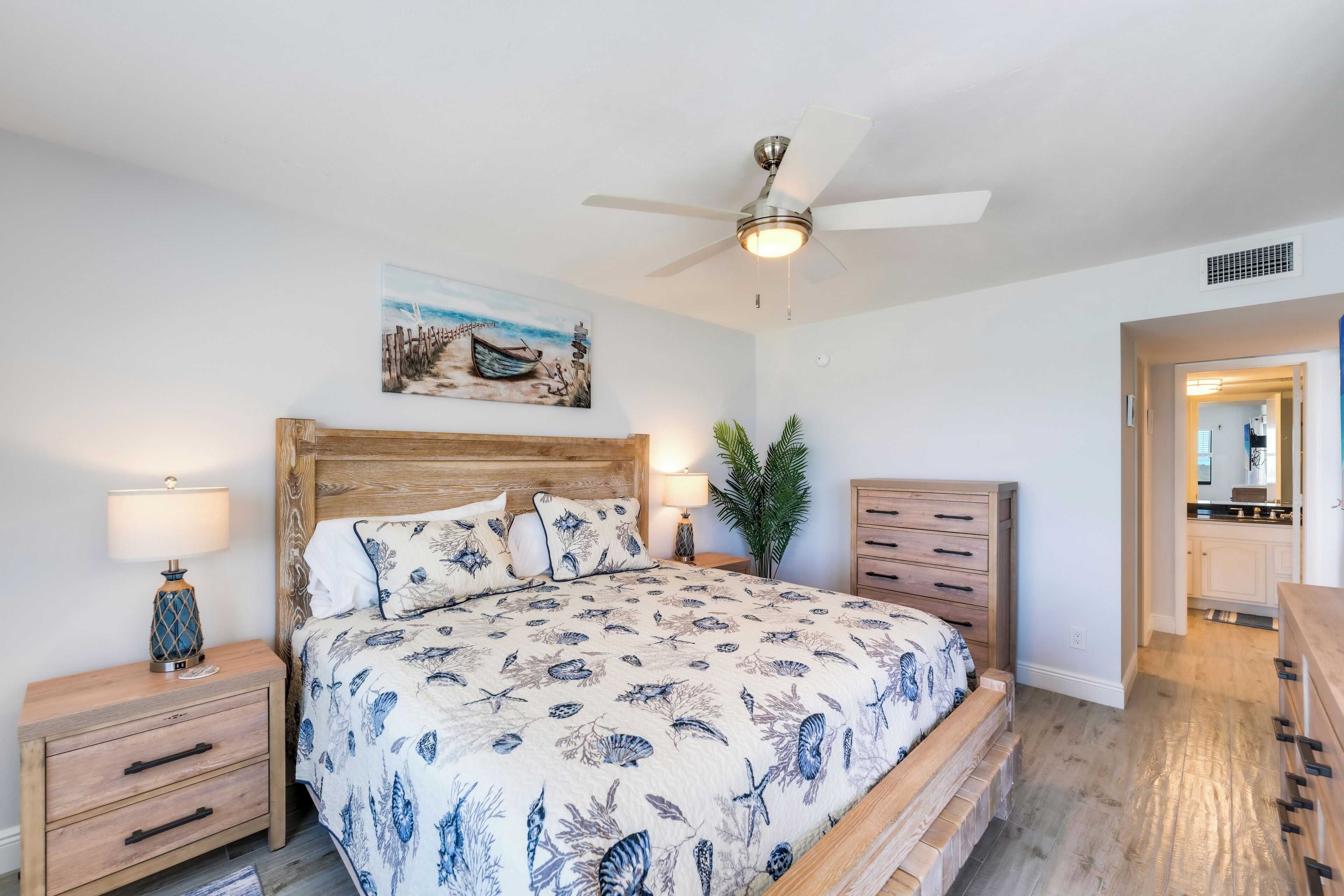 A bedroom with a wooden bed, a ceiling fan, a nightstand with a lamp, and a painting on the wall.