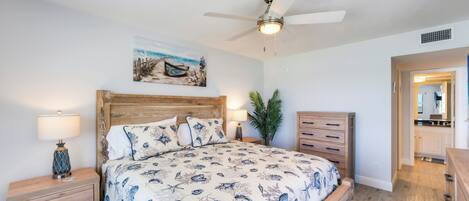 A bedroom with a wooden bed, a ceiling fan, a nightstand with a lamp, and a painting on the wall.