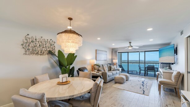 A modern living room with a round marble table, comfortable seating, a chandelier, and a large window offering a view of the ocean. - Gulf View! 2B/2B CONDO AT ISLANDS END 804! Pool! (Fort Myers Beach)