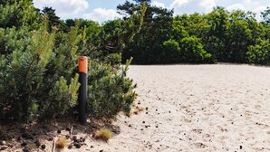 A sandy beach with dense green foliage and a tall orange pole. - Fully furnished apartment with balcony on forest and dune area (Soest)