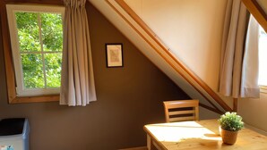A room with a wooden table, a chair, a window with curtains, and a framed picture on the wall. - Fully furnished apartment with balcony on forest and dune area (Soest)