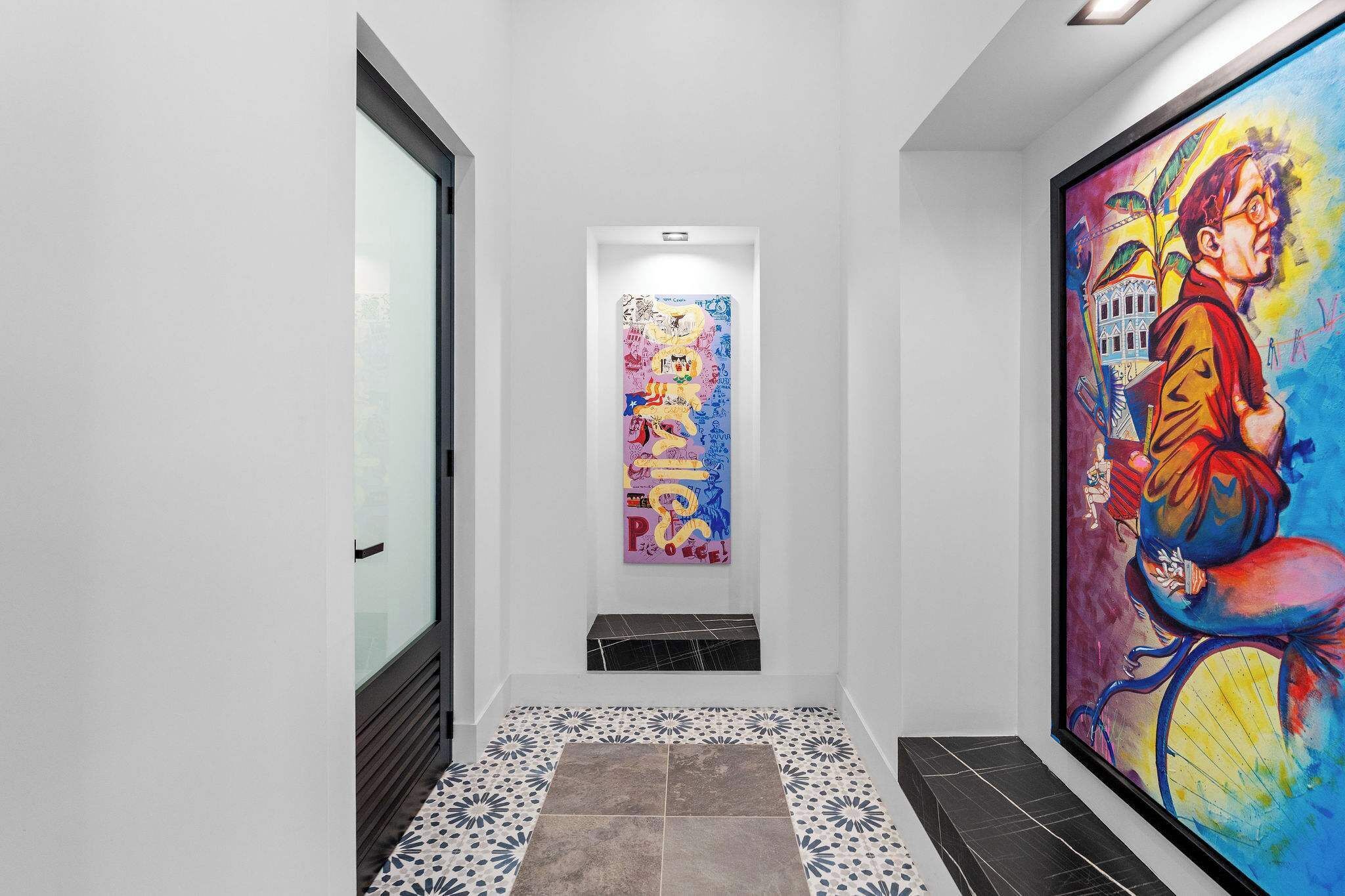 A hallway with a tiled floor, a framed artwork on the right, and a framed artwork on the left.