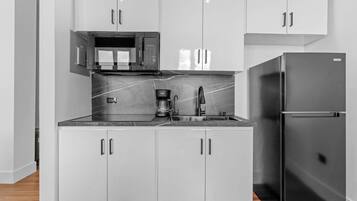Una cocina compacta con armarios blancos, un refrigerador negro, un microondas y una cafetera.