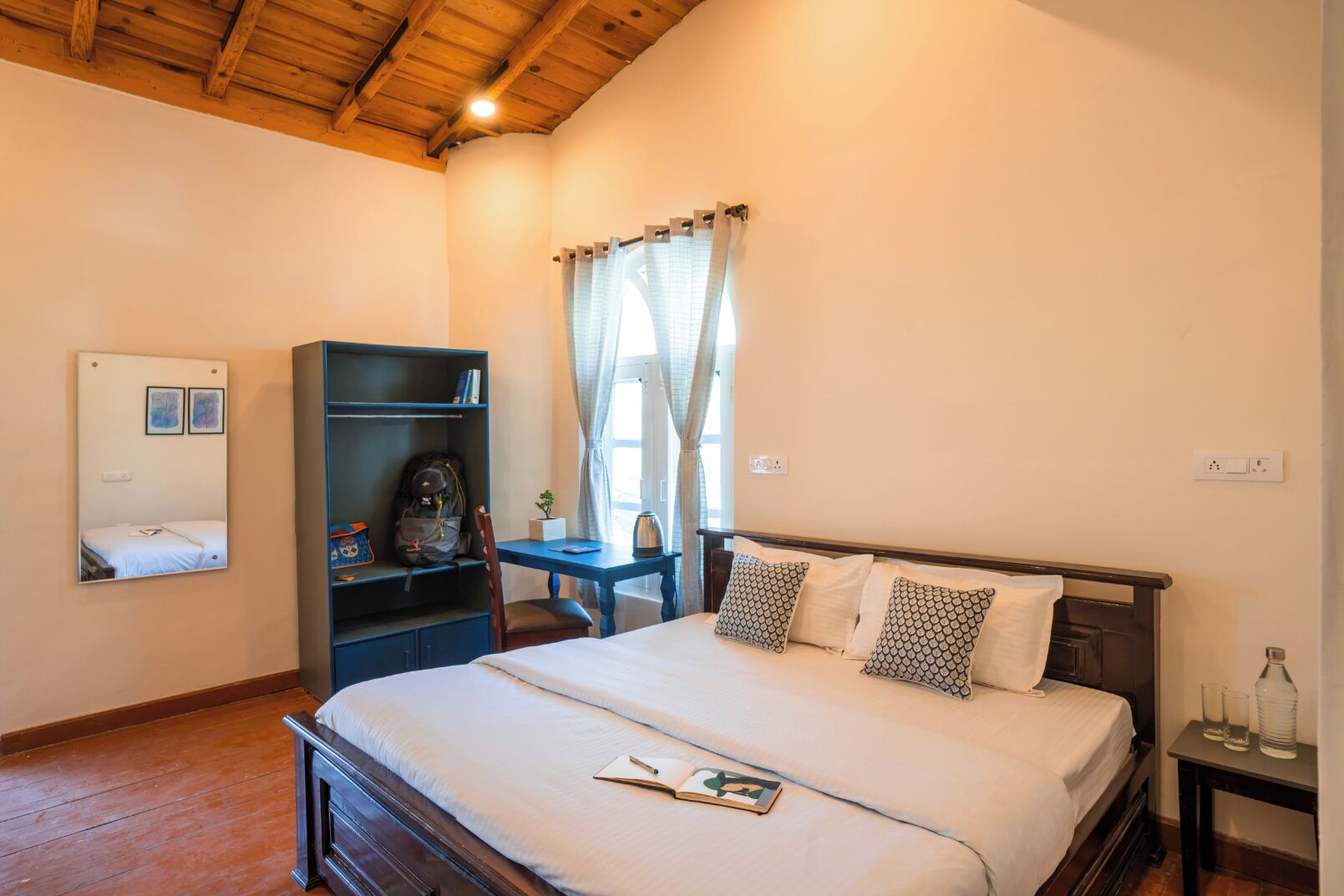 A bedroom with a wooden bed, a desk, a bookshelf, and a window with curtains.