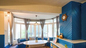 Une pièce avec une table ronde, des bancs bleus, un plafond en bois et un gouvernail de bateau accroché au mur.