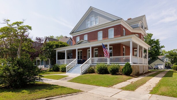 A two-story brick house with a front porch, a flag, and a well-maintained lawn.