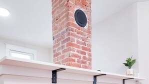 A kitchen with a brick chimney, white shelves, and wooden stools.