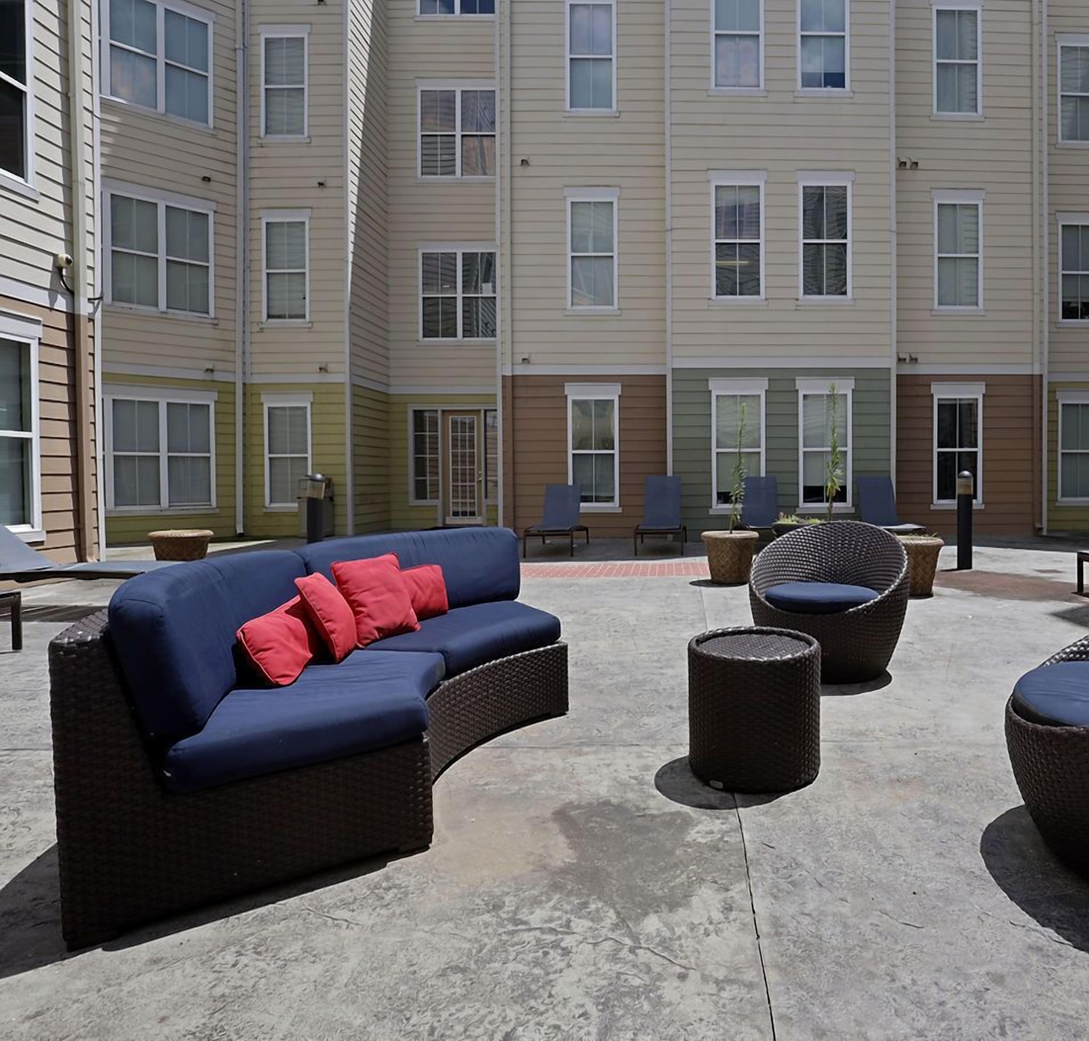 A courtyard with outdoor seating, including a sofa and chairs, and a building with multiple windows in the background.