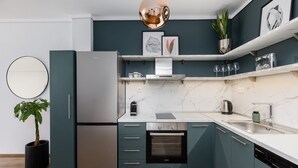 A modern kitchen with teal cabinets, a stainless steel refrigerator, a built-in oven, and a marble countertop. - Aurora by halu (Thessaloniki)