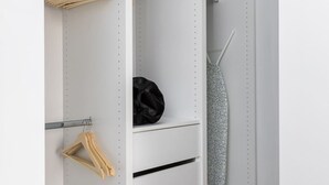 A white wardrobe with multiple shelves and hanging space, including wooden hangers and a black bag. - Aurora by halu (Thessaloniki)