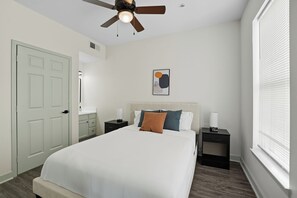 A bedroom with a bed, nightstands, a ceiling fan, a window with blinds, and a door. - Spacious 2-Bedroom Apartment in Memphis (Memphis)