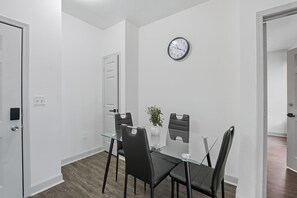 A modern dining area with a glass table, black chairs, a potted plant, and a wall clock. - Spacious 2-Bedroom Apartment in Memphis (Memphis)