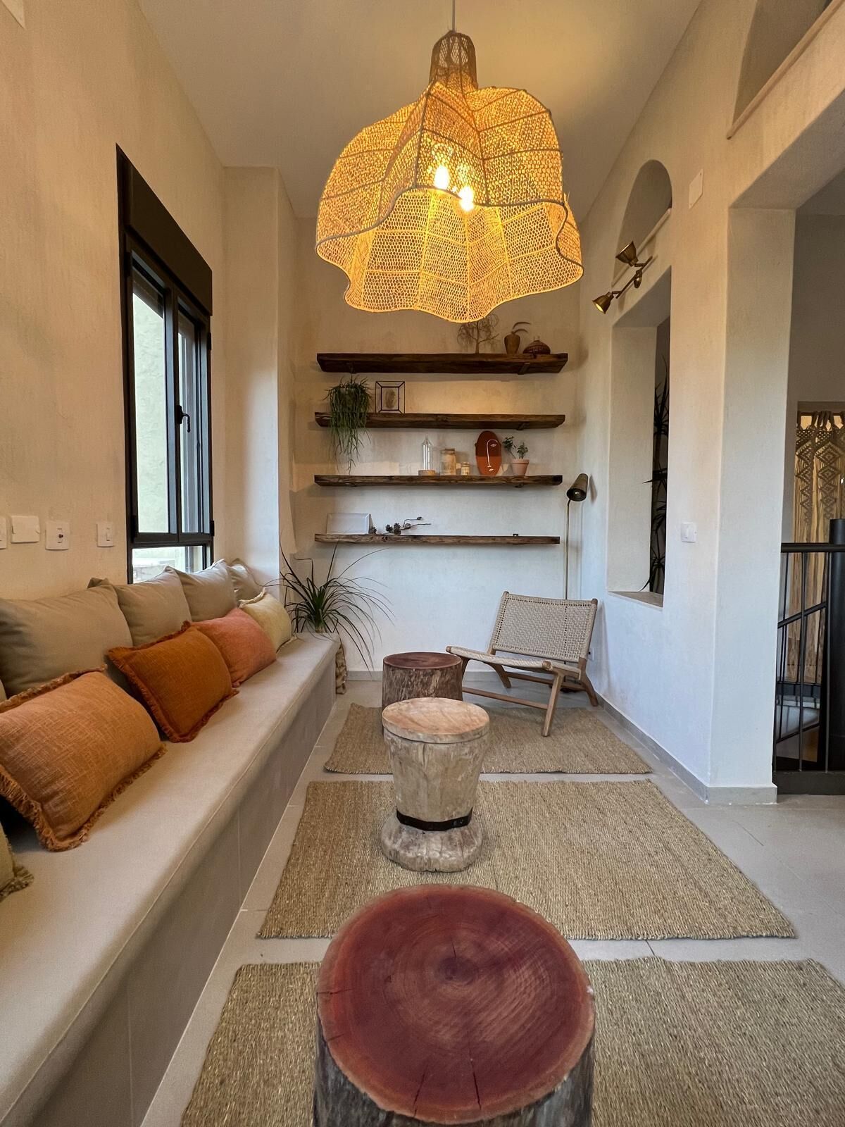A living room with a sofa, a round wooden stool, a hanging light fixture, and shelves with decorative items.
