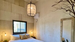 Ein Schlafzimmer mit einem großen Bett, einem Fenster, einer Pendelleuchte und einer Wand-Klimaanlage.