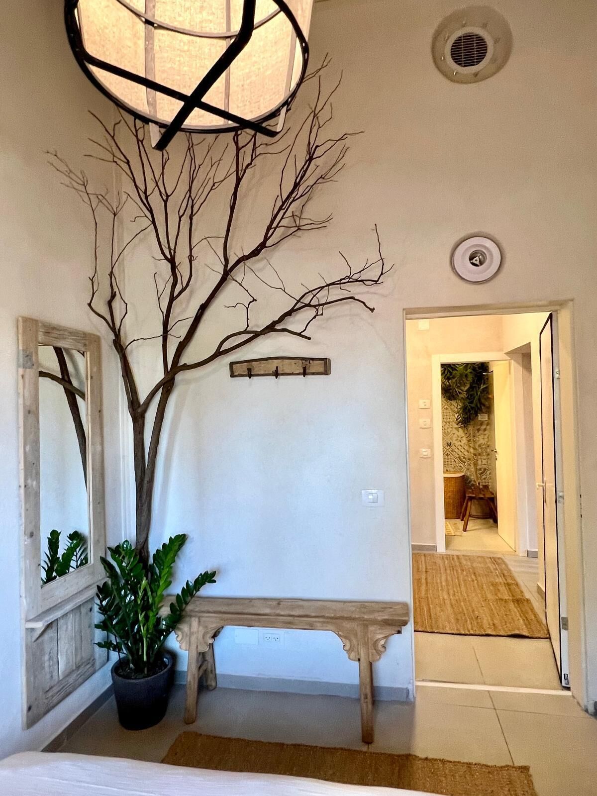 Un couloir avec un banc en bois, une sculpture représentant un arbre sans feuilles et un luminaire fixé au mur.