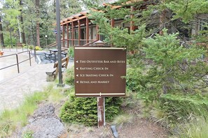 Un cartel con indicaciones hacia The Outfitter Bar and Bites, Registro de Rafting, Registro de Patinaje sobre Hielo y Tienda y Mercado.