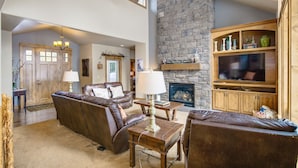 A spacious living room with leather sofas, a stone fireplace, and a wooden entertainment center. - 56540 Sunstone Loop- Caldera Springs - A/C, Hot Tub, Gas Fire Pit! (Sunriver)