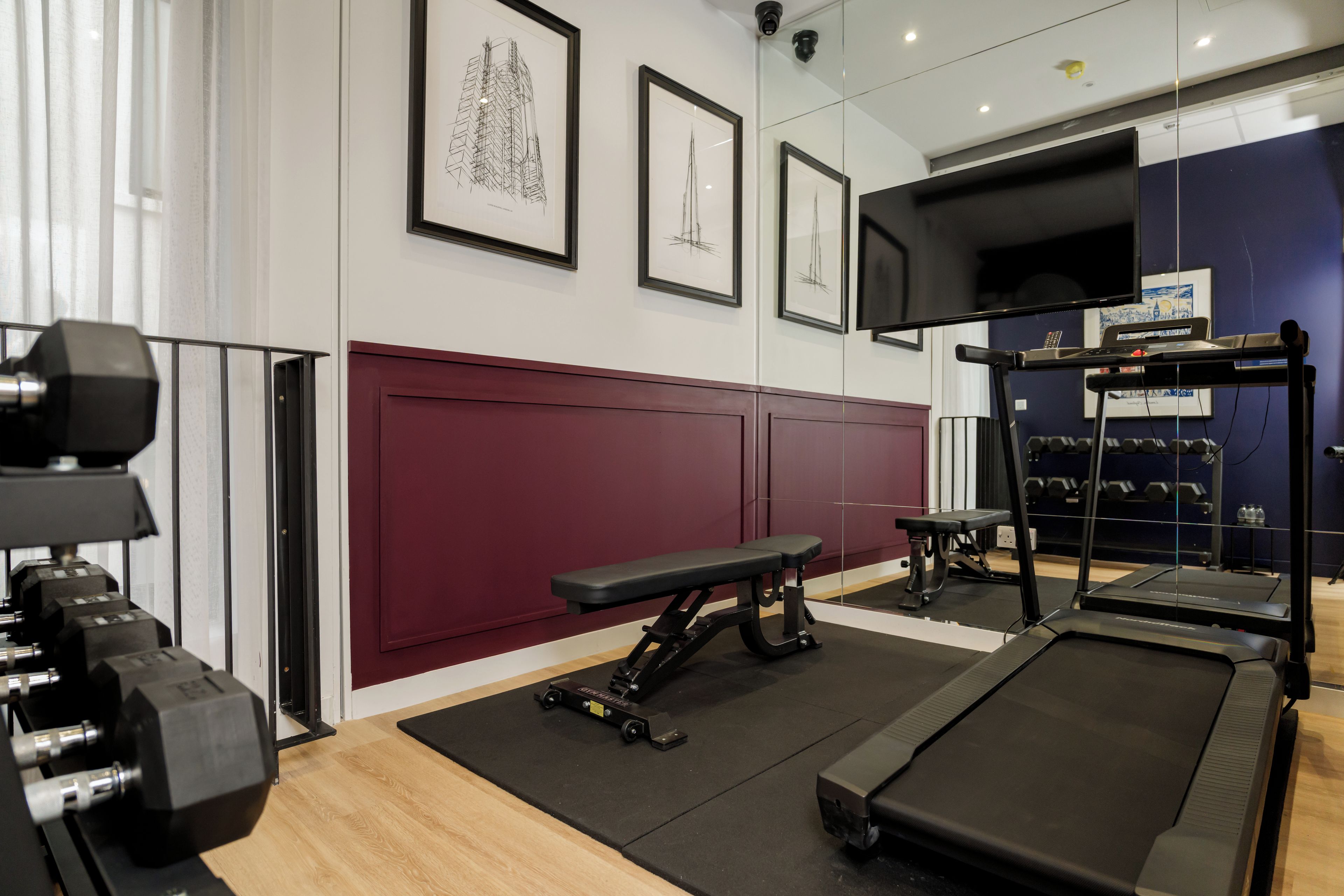 A gym with exercise equipment, a bench, treadmills, and framed artwork on the walls.