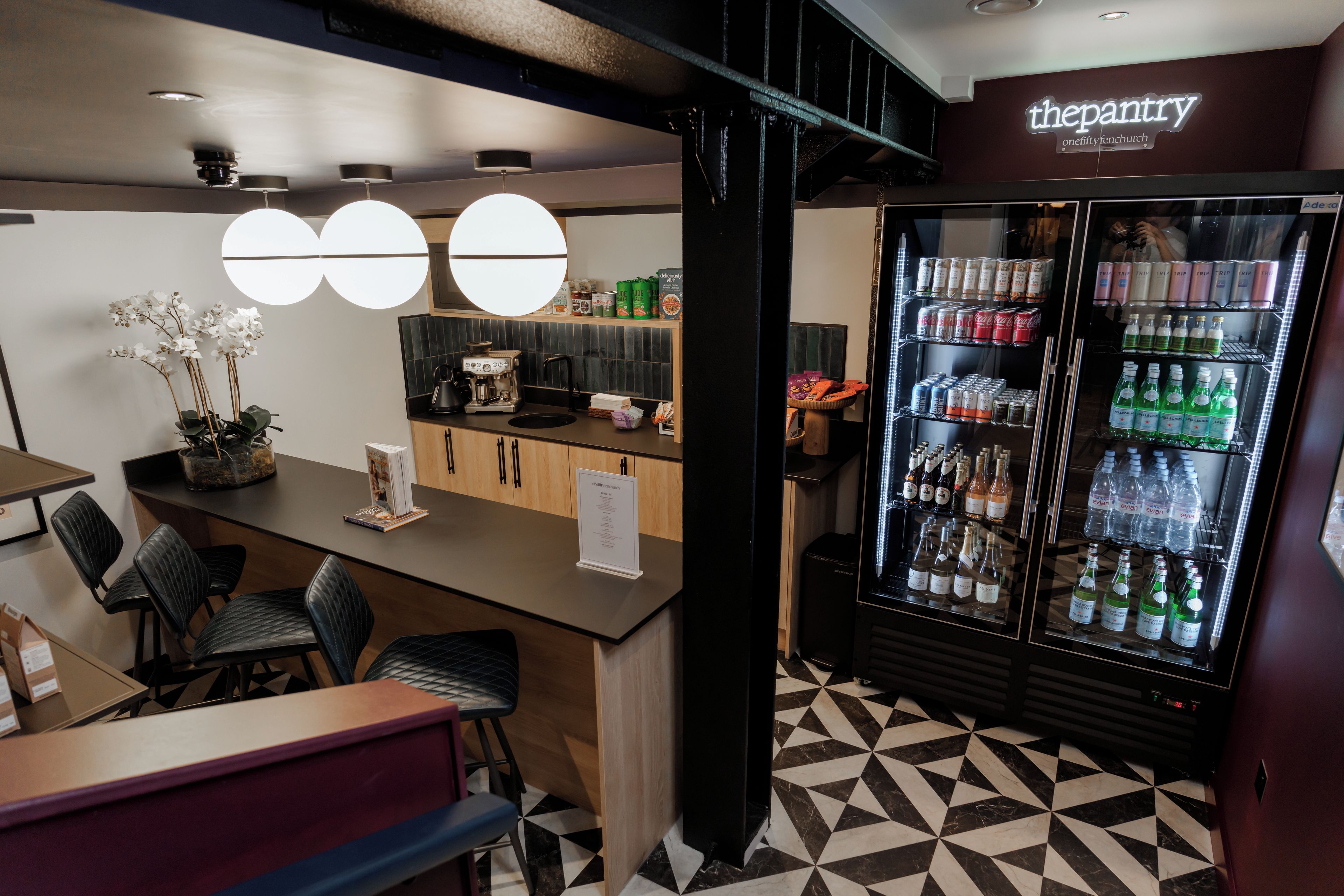 A café interior with a bar area, seating, a coffee machine, and a beverage refrigerator stocked with drinks.