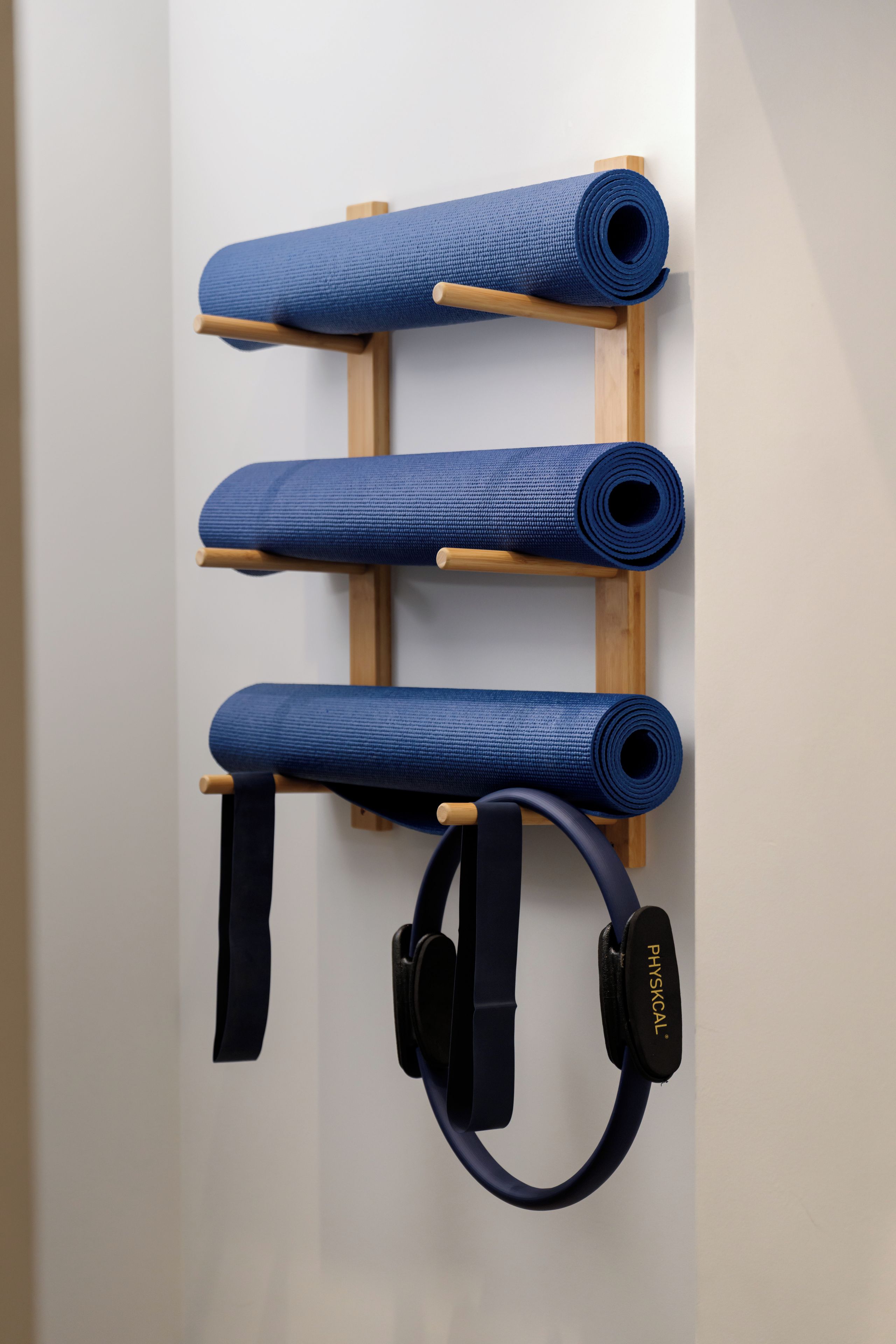 Ein an der Wand befestigter Träger mit drei aufgerollten Yogamatten und einem Yoga-Gurt.