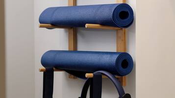 Ein an der Wand befestigter Träger mit drei aufgerollten Yogamatten und einem Yoga-Gurt.