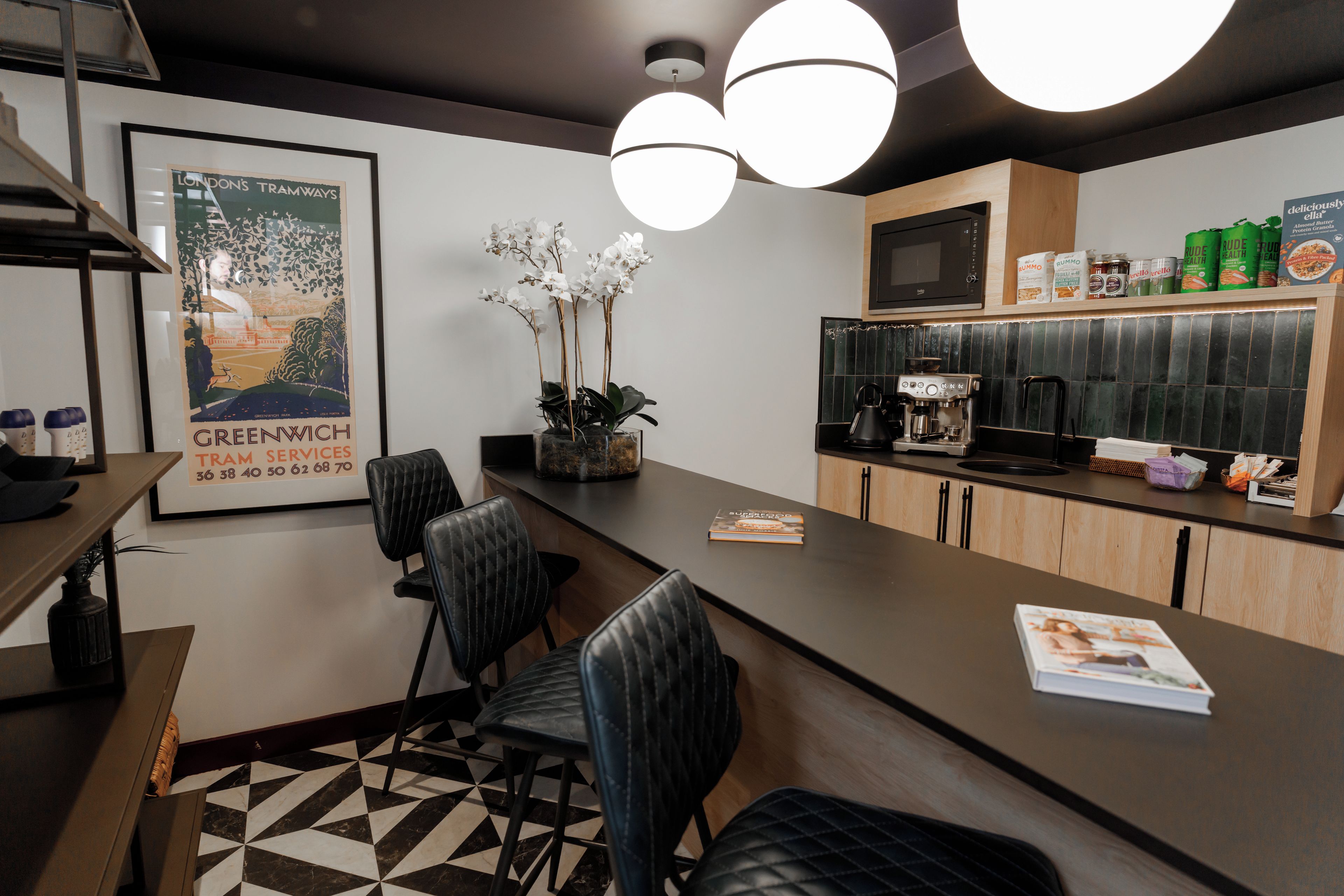 A modern kitchen with a bar area, a coffee machine, and a framed poster on the wall.