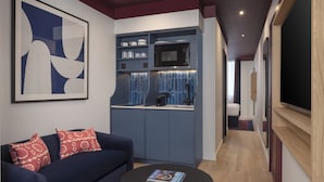 Un salon moderne avec un canapé bleu foncé, une table basse ronde et un coin cuisine doté de meubles bleus et d’un four à micro-ondes.