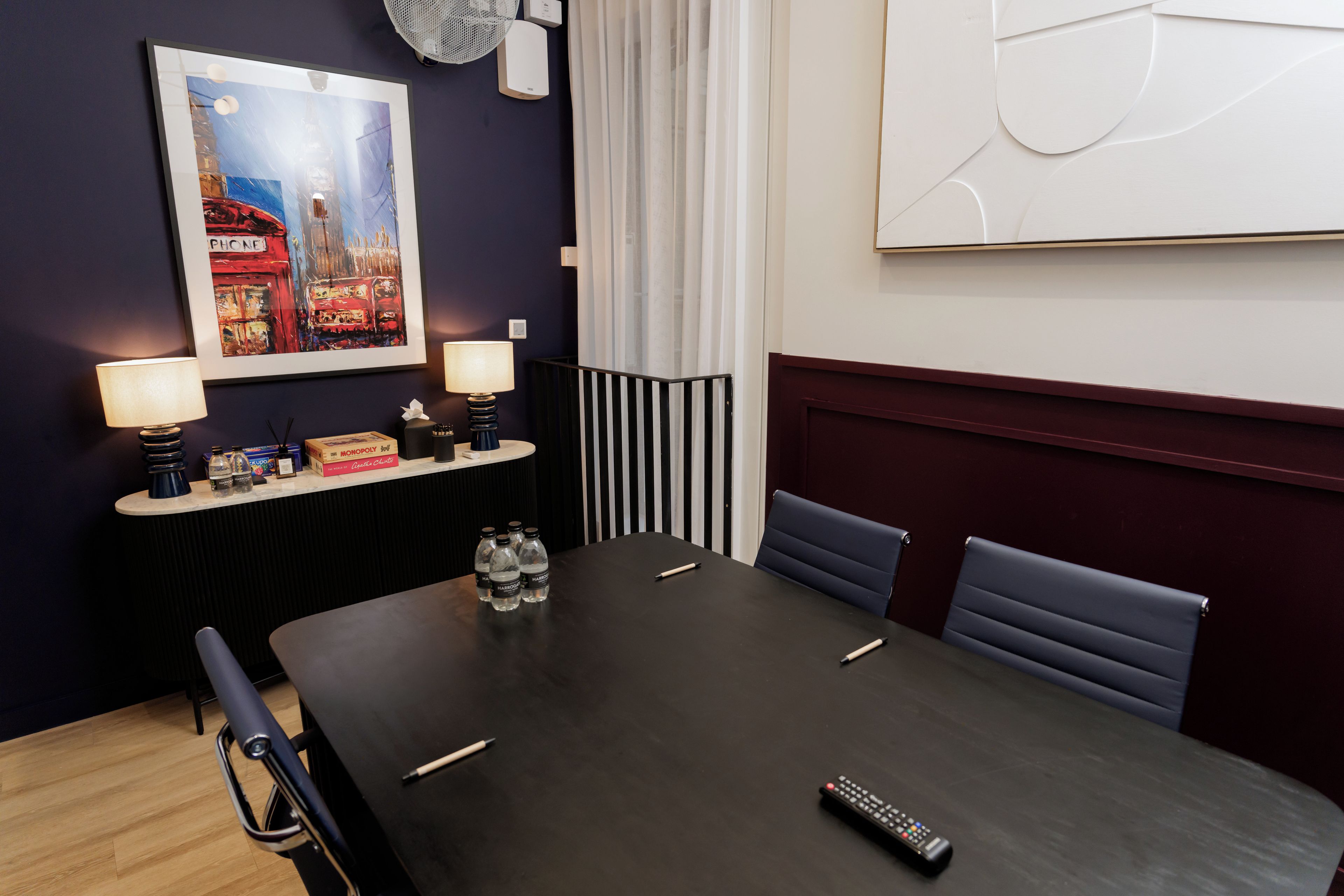A conference room with a dark table, chairs, a remote control, and a framed artwork on the wall.