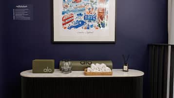 Ein gerahmtes Kunstwerk von London, England, an einer dunklen Wand. Darunter ein Tisch mit einem grünen Laptop, Wasserflaschen, einem Diffusor und zusammengerollten Handtüchern vor dunklem Hintergrund.