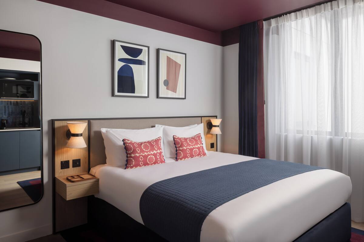A hotel room with a large bed, two bedside lamps, a nightstand, a mirror, and two framed artworks on the wall.