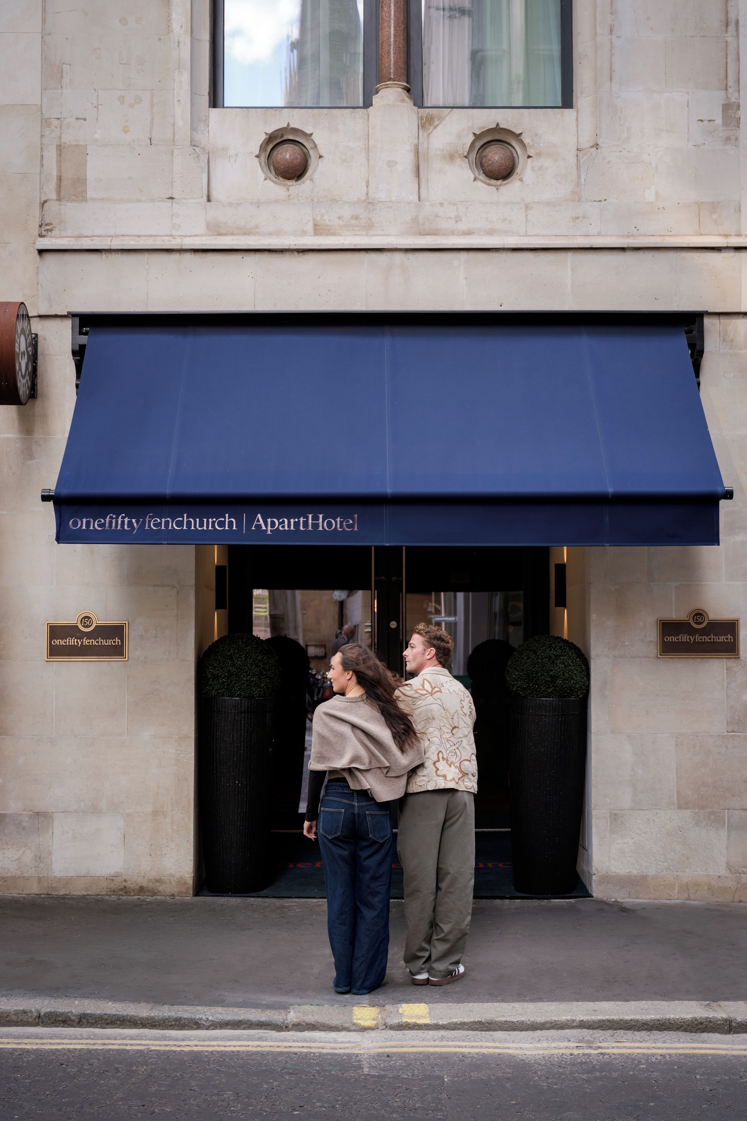 A building with a blue awning, two black doors, and a sign reading 'onefifty fenchurch | ApartHotel'.