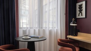 Une pièce avec une table ronde, deux chaises, une lampe, un tableau encadré et des rideaux légers.