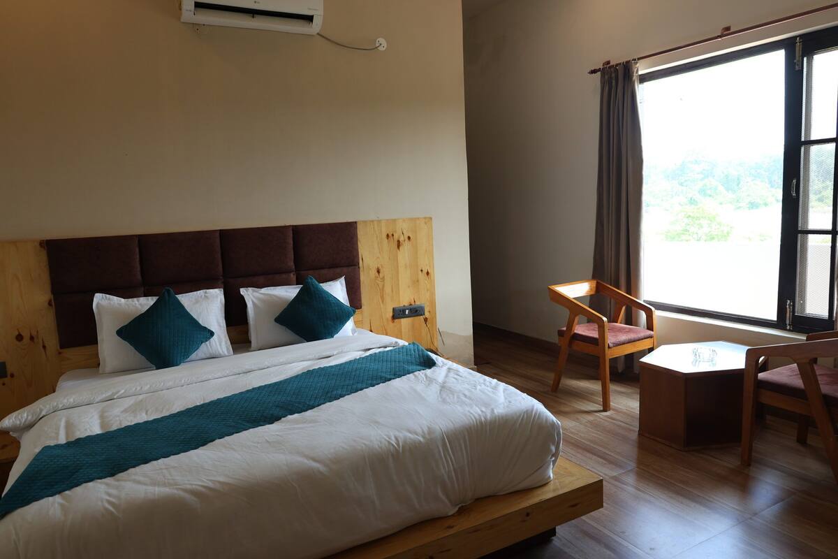 A hotel room with a bed, a chair, a small table, and a window with a view.