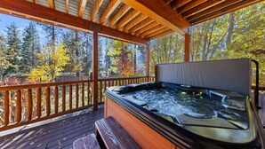 Un patio in legno con una vasca idromassaggio, ringhiere in legno e vista sugli alberi.