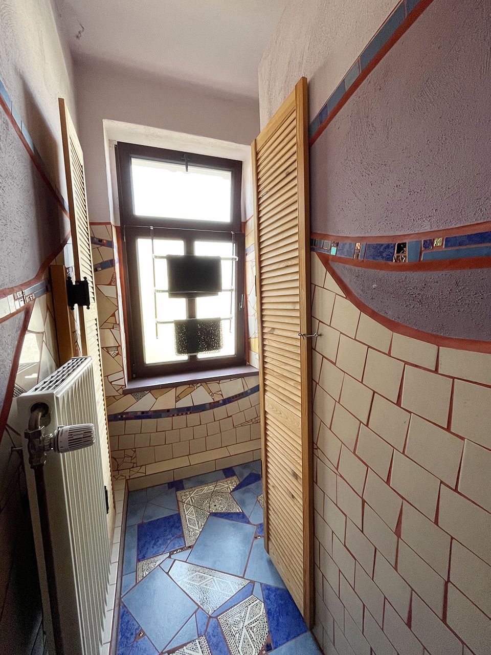 Un baño estrecho con ventana, suelo de baldosas y un radiador.