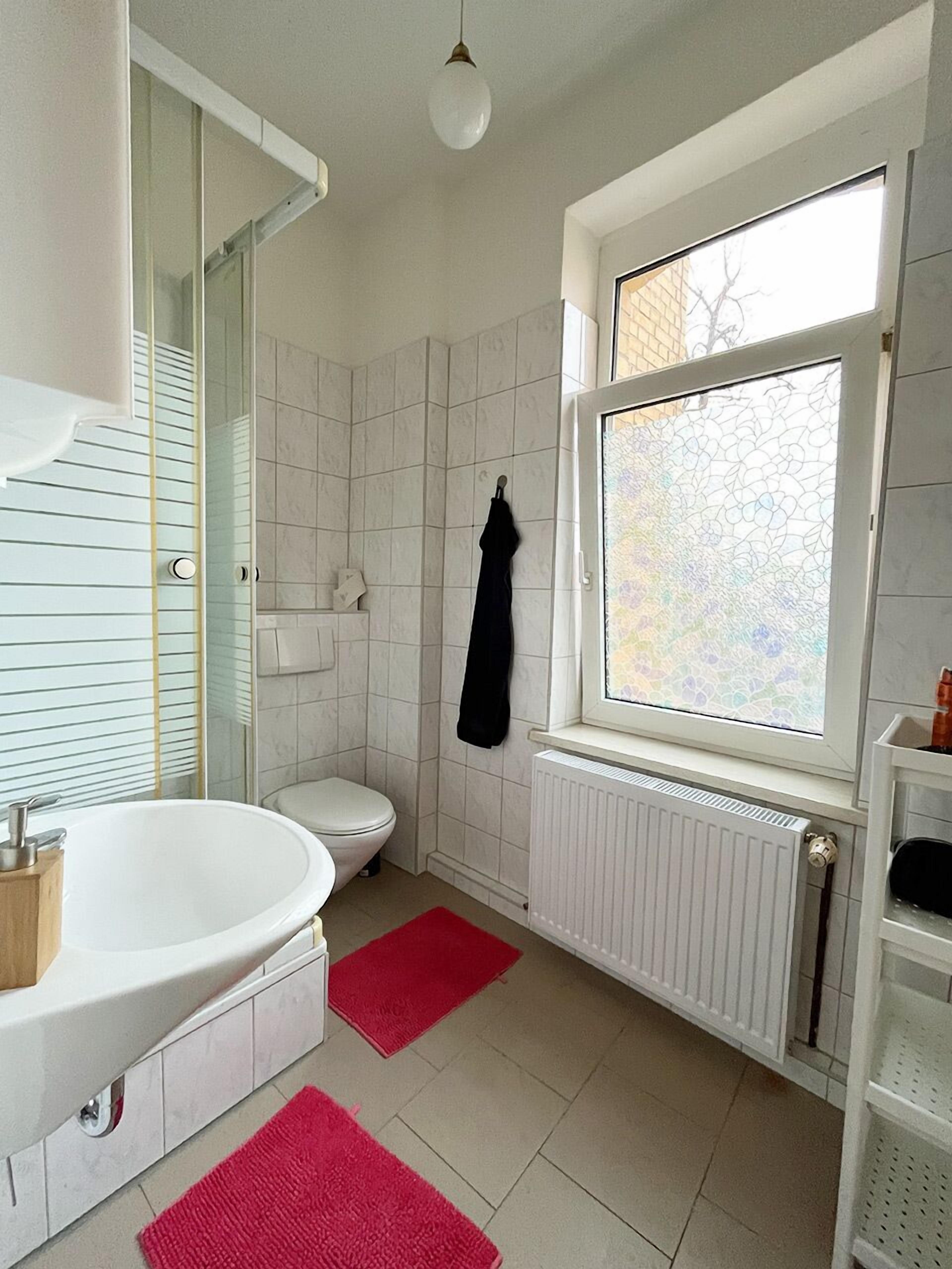 Un baño con una bañera blanca, inodoro y ventana con vistas a árboles.