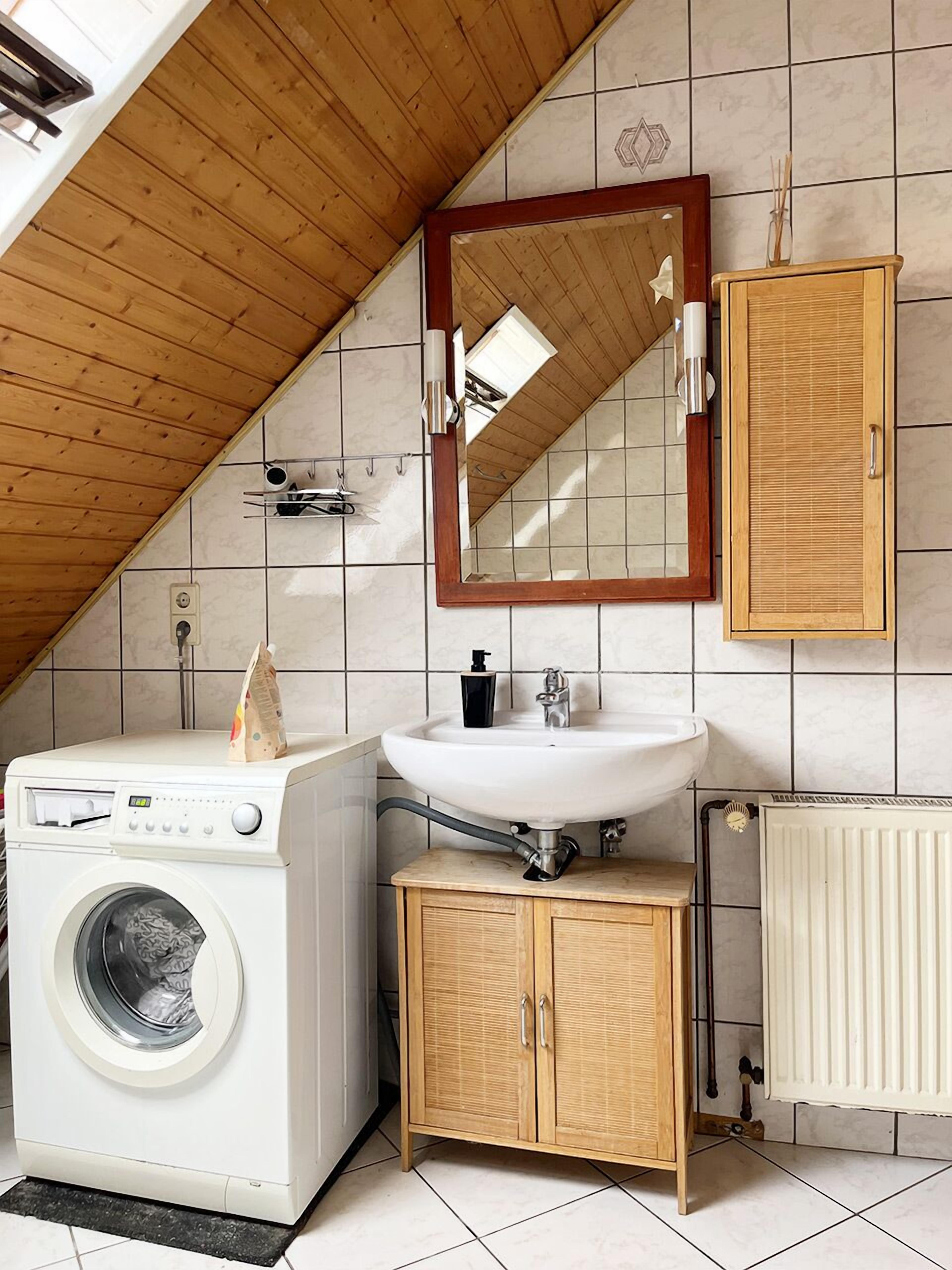 A compact, modern bathroom with a wooden ceiling, a built-in washing machine, a sink, and a cabinet.