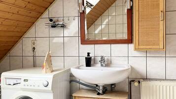 A compact, modern bathroom with a wooden ceiling, a built-in washing machine, a sink, and a cabinet.