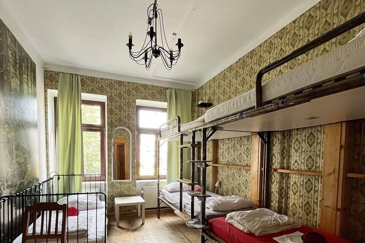 A dormitory room with bunk beds, a wooden desk, a chair, and a chandelier.