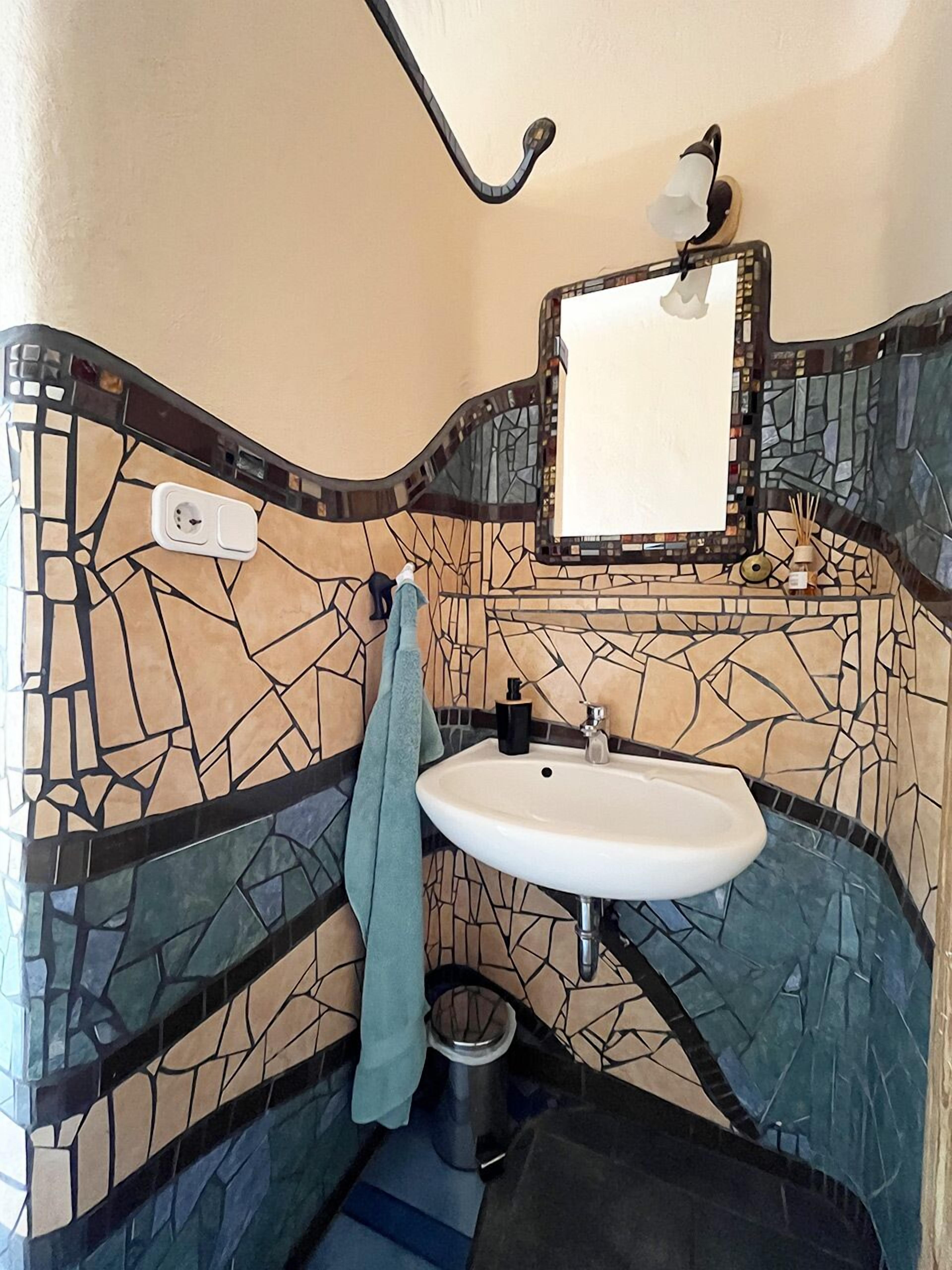 A bathroom with a mosaic tile wall, a white sink, a towel, and a mirror.