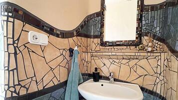 A bathroom with a mosaic tile wall, a white sink, a towel, and a mirror.