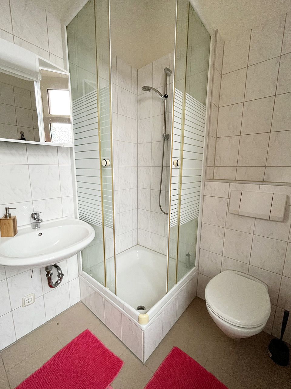 Un baño moderno con ducha de vidrio, un lavamanos blanco y un inodoro.