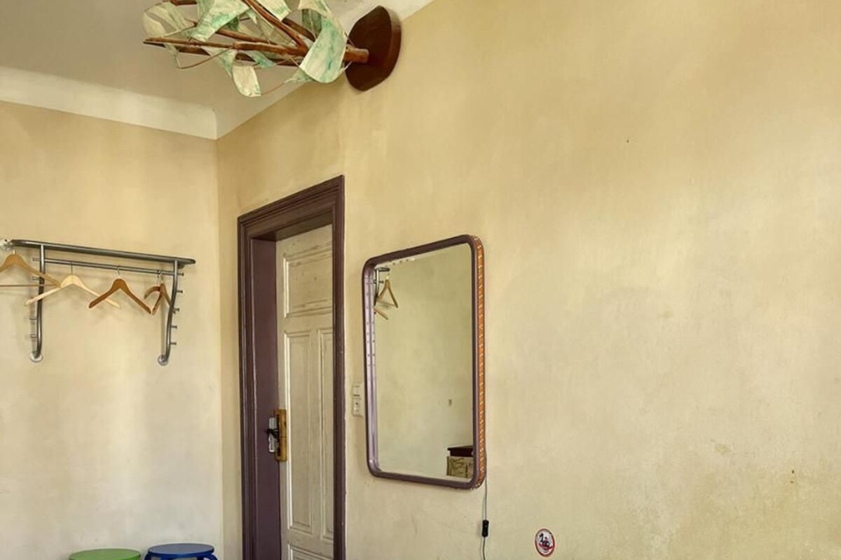 Un dormitorio con cama, espejo, puerta y perchero.